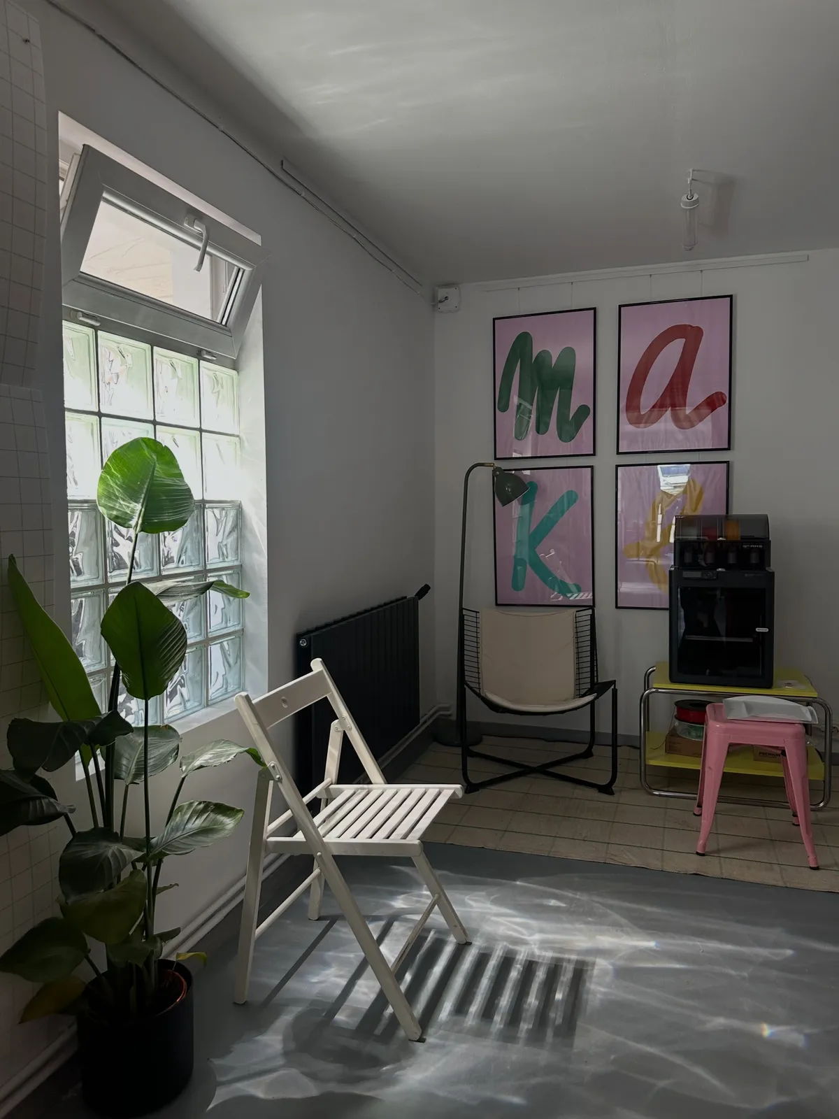 Sunlit corner with a glass-block window, a white chair and MAKE letter posters